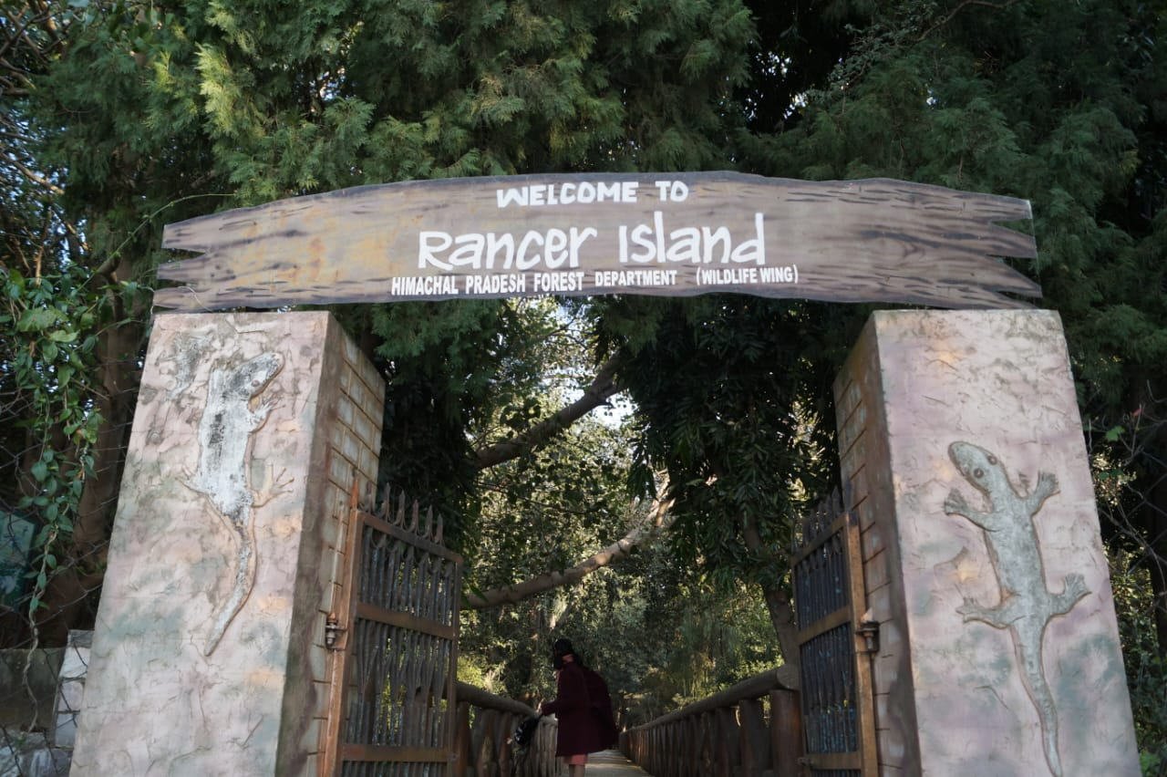 The Himachal Pradesh Forest Department welcome gate on Rancer Island, with a visitor walking through onto the island path